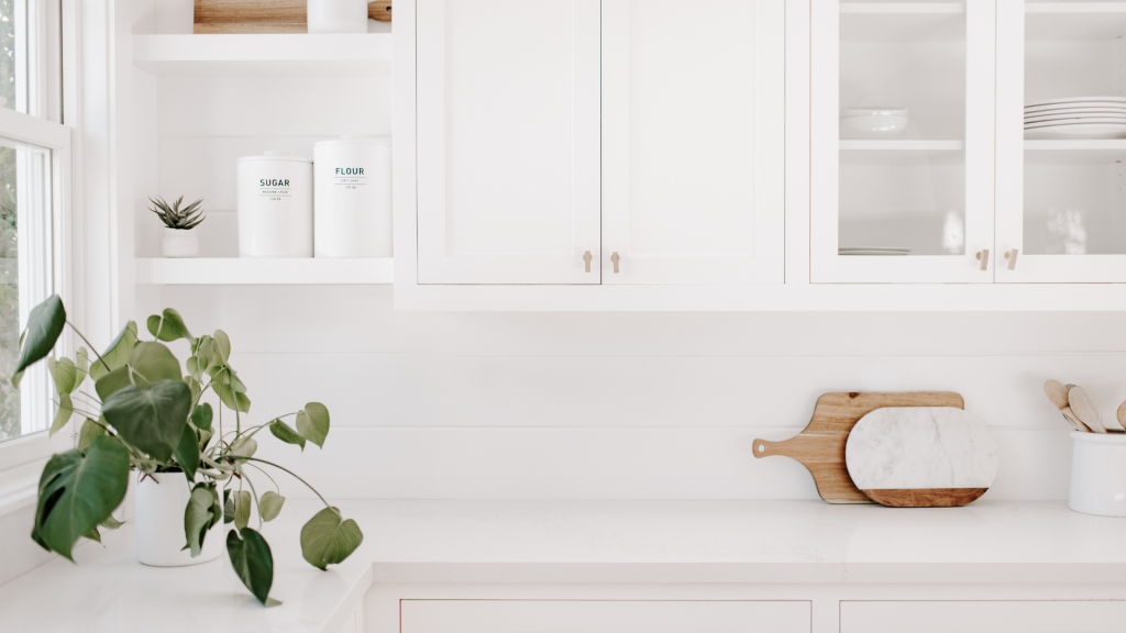 a white minimalist kitchen with clear worktops and a plant